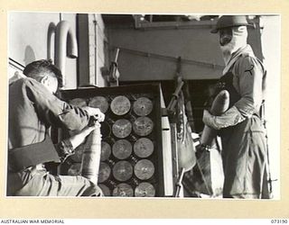 OFF NEW GUINEA COAST. 1944-05. A MEMBER OF A GUN CREW ABOARD HMAS KAPUNDA REFILLS THE "READY USE" AMMUNITION WHILE ANOTHER MEMBER STANDS READY TO PASS A SHELL TO THE 4 INCH GUN DURING A LULL IN THE ..