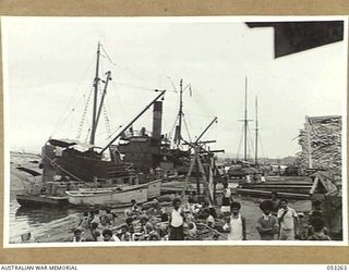 MILNE BAY, NEW GUINEA. 1943-06-30. THE "MARRAWAH", AN AMERICAN SUPPLY SHIP WHICH SUPPLIES THE TROOPS ON THE VARIOUS ISLANDS, LOADS AT THE PONTOON WHARF. IN THE BACKGROUND IS THE SUNKEN VESSEL ..