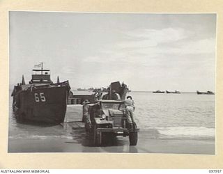 WEWAK BEACH, NEW GUINEA. 1945-10-18. A SUPPLY TRUCK BACKING ONTO A LANDING CRAFT, TANK (LCT) WHICH HAS BEEN LOADED WITH STORES FROM CARGO SHIP. MEMBERS OF 8 PORT OPERATING COMPANY SUPERVISE ..