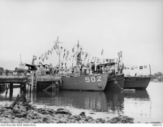JACQUINOT BAY, NEW BRITAIN, 1945-08-15. NAVY LAUNCH ML502 AND OTHER SMALL CRAFT WITHIN THE PORT DIRECTORATE FLYING ALL FLAGS AND BUNTING INCLUDING THE PIRATE JOLLY ROGER (SKULL AND CROSS-BONES) ..