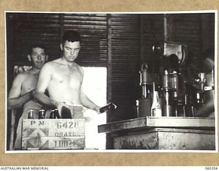 17 MILE, LALOKI RIVER, NEW GUINEA. 1943-11-22. NX43473 PRIVATE E. PIDGEON (LEFT) AND N45506 PRIVATE W. LOY (RIGHT) REMOVING BOTTLES FROM THE FILLING MACHINE AND PACKING THEM FOR DELIVERY TO UNITS ..