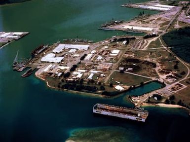 An aerial view of various ships moored in the harbor, with a floating dry dock in the foreground