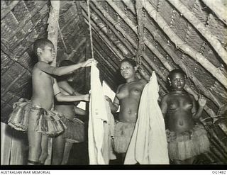 KIRIWINA, TROBRIAND ISLANDS, PAPUA. C. 1944-03. LOCAL PAPUAN NATIVE WOMEN JILL TOOTS, MATILDA AND JOSEPHINE, HANG WASHING IN A NATIVE BUILT HUT USED AS A DRYING ROOM AT NO. 46 OPERATIONAL BASE UNIT ..