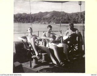 Three ships officers aboard Fairmile Motor Launch ML 426 enjoy a quiet interlude between assignments. Identified personnel are Sub Lieutenant Peter Ailwood (1); Sub Lieutenant Dudley Ross (2); ..