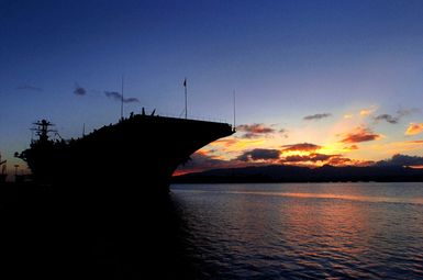 The sun sets behind the US Navy (USN) Nimitz Class Aircraft Carrier USS JOHN C. STENNIS (CVN 74) as she sits pier side in Pearl Harbor, Hawaii. The STENNIS and Carrier Air Wing 14 (CVW-14) are taking part in Rim of the Pacific (RIMPAC) 2004. RIMPAC is the largest international maritime exercise in the waters around the Hawaiian Islands. This years exercise includes seven participating nations: Australia, Canada, Chile, Japan, South Korea, the United Kingdom and the United States. RIMPAC enhances the tactical proficiency of participating units in a wide array of combined operations at sea, while enhancing stability in the Pacific Rim region