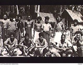 REINHOLD HIGHWAY, NEW GUINEA, 1943-08-31. NATIVE ROAD WORKERS OUTSIDE THE AUSTRALIAN AND NEW GUINEA ADMINISTRATION UNIT HEADQUARTERS HUT WAITING FOR THEIR LEAVE PASSES