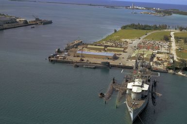 An elevated bow view of the submarine tender USS PROTEUS (AS 19) moored at Polaris Point, with submarines positioned alongside