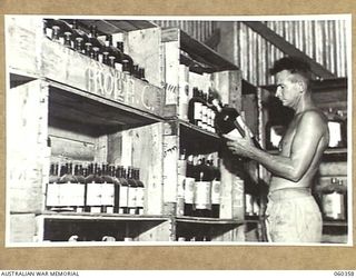 17 MILE, LALOKI RIVER, NEW GUINEA. 1943-11-22. QX15721 CORPORAL J. PEUT CHECKING SUPPLIES OF ESSENCES IN THE STORE OF THE CORDIAL FACTORY ESTABLISHED AND OPERATED BY THE AUSTRALIAN DEFENCE CANTEEN ..