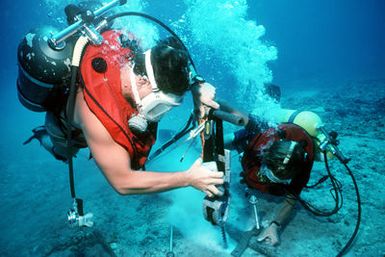 Divers work against the current to repair an undersea cable at the Pacific Missile Range Facility. Steelworker Second Class (SW2) David Patterson (left) uses a hydraulic drill with assistance from Construction Electrician Second Class (CE2) Todd Horne. Both divers are members of Underwater Construction Team 2, Port Hueneme, California