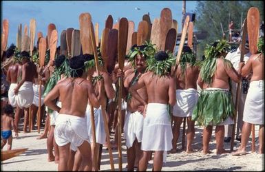 Groups of men in white maro and pāreu holding wooden paddles