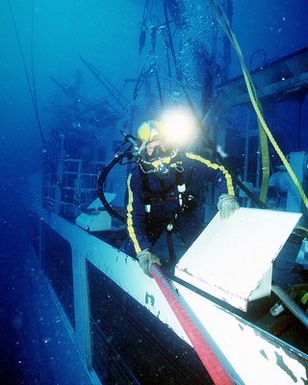 A US Navy diver assigned to Mobile Diving and Salvage Unit One (MDSU-1 pulls a vacuum hose across the deck of Ehime Maru, during recovery operations for the Japanese fishing vessel Ehime Maru off the coast of Hawaii