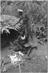 Pig festival, pig sacrifice, Tsembaga: ritual exchange of shell valuables, steel axes, and other wealth displayed on mat, man holds leg of pork