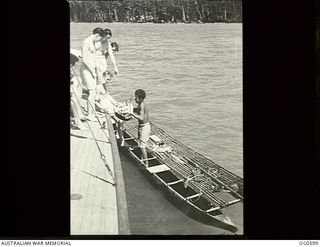 TROBRIAND ISLANDS, PAPUA. C. 1944. A NEW GUINEA NATIVE BOY HANDS UP A DISH OF BANANAS TO RAAF MEMBERS 8326 LEADING AIRCRAFTMAN (LAC) JACK HURRY OF MELBOURNE, VIC; 407468 FLYING OFFICER M. E. TOWILL ..