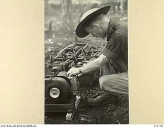 KILIGIA, NEW GUINEA, 1944-03-12. NX4174 SIGNALMAN J. WALKER (1) AT HEADQUARTERS 5TH DIVISION SIGNALS, USING A 12 VOLT 300 WATT "JOHNSON CHORE HORSE", TO CHARGE BATTERIES IN THE FIELD