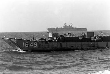 Marines of the 2nd Light Armored Infantry Battalion, 4th Marine Regiment, ride toward Vieques, Puerto Rico, aboard the utility landing craft LCU-1649 during Fleet Ex 1-90. In the background is the amphibious assault ship USS SAIPAN (LHA-2)