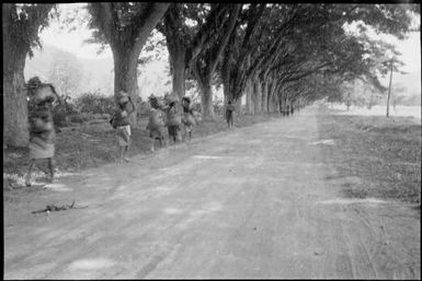 Woman carrying a bag on her head and two women with bilums walking to the Boong, native markets, Rabaul, New Guinea, ca. 1936 / Sarah Chinnery