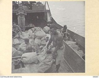 CAPE WOM, WEWAK AREA, NEW GUINEA. 1945-09-06. NATIVE BOYS, ABOARD AN ARMY BARGE, LOADING MAIL INTO TRUCKS 6 DIVISION POSTAL UNIT