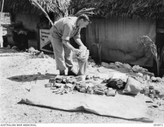 PALMALMAL PLANTATION, JACQUINOT BAY, NEW BRITAIN, 1945-07-13. CORPORAL E.J. PICKERING, AUSTRALIAN COMFORTS FUND, 5 BASE SUB-AREA, ASSISTING THE YOUNG MEN'S CHRISTIAN ASSOCIATION BY PLACING ..