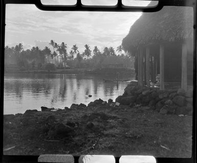 Unidentified man on boat at Faleolo, Apia, Upolu, Samoa, showing fales and palm trees