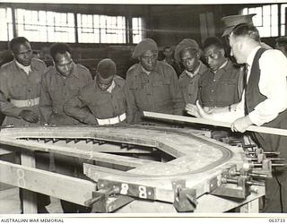 ALEXANDRIA, NSW. 1944-01-24. AUSTRALIAN AND NEW GUINEA ADMINISTRATION UNIT NATIVES BEING SHOWN THE METHODS USED IN THE CONSTRUCTION OF LAMINATED RIBS FOR PLYWOOD LANDING BARGES AT SLAZENGER'S ..