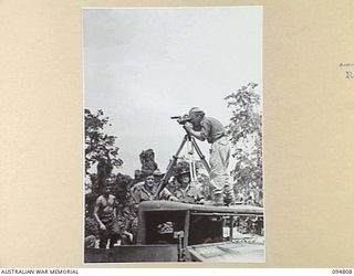 TOROKINA AREA, BOUGAINVILLE, 1945-08-08. LIEUTENANT WOOD OPERATING A BELL AND HOWELL TURRET EYEMO MOUNTED ON A TRIPOD ON THE ROOF OF A TRUCK. HE IS FILMING AN M24 GENERAL CHAFFEE LIGHT TANK DURING ..