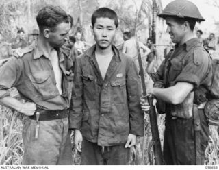 DUMPU, NEW GUINEA. 1943-10-05. SX123484 LANCE SERGEANT N. B. STUCKEY, AUSTRALIAN MILITARY HISTORY SECTION PHOTOGRAPHER (LEFT), CLOSELY EXAMINES A JAPANESE PRISONER CAPTURED BY SX12395 LANCE ..