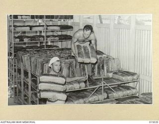 1943-06-15. NEW GUINEA. A.I.F. BAKERS AT WORK IN NEW GUINEA. PTE. N. BLACKSHAW, OF WEST RYDE, N.S.W. SGT. A. JENKINS OF INVERELL, N.S.W. TAKE BROAD FROM THE COOLING RACKS. (NEGATIVE BY N. BROWN)