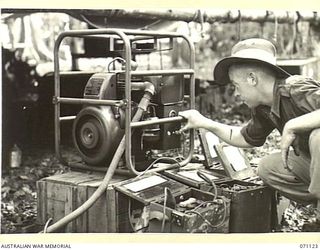 KILIGIA, NEW GUINEA. 1944-03-12. QX57857 SIGNALMAN J. V. DAVIDSON (1), OF HEADQUARTERS, 5TH DIVISION SIGNALS, STARTING THE MOTOR TO CHARGE WIRELESS ACCUMULATORS USING THE "ONAN" 1260 BATTERY ..