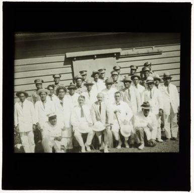 Military personnel and civilians standing in front of wooden building