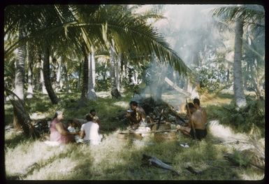 Members of the Marsters' Third Family eating a meal in a clearing among palm trees, on Palmerston Island, Cook Islands