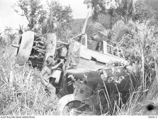 BUT, NEW GUINEA. 1945-04-02. SERGEANT C.R. GILL, 2/6 TRANSPORT PLATOON (1), EXAMINING A "SONIA" JAPANESE RECONNAISSANCE AIRCRAFT DESTROYED BY ALLIED AIR ATTACKS ON THE AIRSTRIP