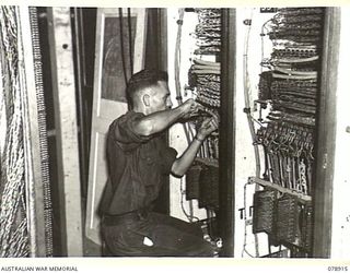 LAE, NEW GUINEA. 1945-02-06. NX39039 SIGNALLER K. JOHNS DOING A MAINTENANCE CHECK ON A SWITCHBOARD AT THE SIGNALS TRANSMITTING CENTRE, 19TH LINES OF COMMUNICATION SIGNALS, HEADQUARTERS, FIRST ..