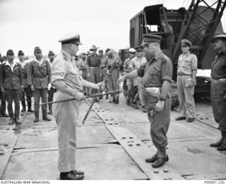 THE SOLOMON ISLANDS, 1945-09-08. BRIGADIER J. FIELD, COMMANDER 7TH AUSTRALIAN BRIGADE, AND A NAVAL OFFICER, WATCHED BY ALLIED AND JAPANESE SERVICE PERSONNEL, EXAMINE TWO JAPANESE SWORDS AT ..