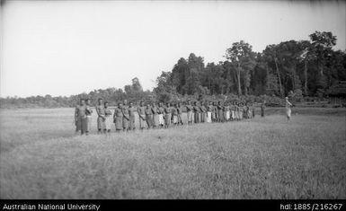 Thirty six men in a field with a European man in a hat