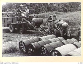 LAE AREA, NEW GUINEA. 1945-07-12. MEMBERS OF 2 BULK PETROLEUM STORAGE COMPANY USING MECHANICAL DRUM SKIDS TO LOAD 44-GALLON DRUMS OF MOTOR SPIRIT