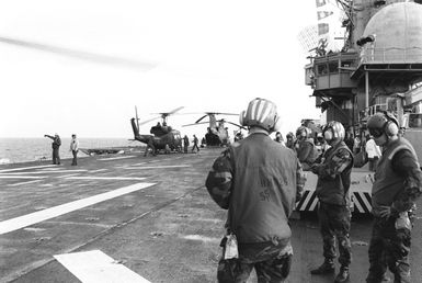Flight operations take place aboard the amphibious assault ship USS GUAM (LPH 9) off the coast of Grenada during Operation URGENT FURY. Visible on the flight deck is a UH-1N Iroquois helicopter and a CH-46 Sea Knight helicopter