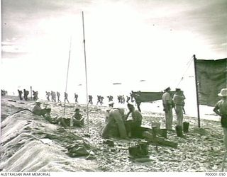 THE SOLOMON ISLANDS, 1945-01-13. BEACH CONTROL SETTING UP AS MORE TROOPS COME ASHORE FROM LANDING CRAFT AT A BOUGAINVILLE ISLAND BEACH. (RNZAF OFFICIAL PHOTOGRAPH.)