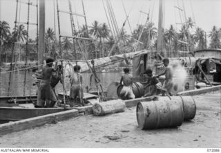 MILNE BAY, NEW GUINEA. 1944-04-06. NEW GUINEA NATIVES LOAD 44 GALLON DRUMS OF PETROL ABOARD THE "KEKERE", AN AUSTRALIAN SMALL CRAFT WHICH DELIVERS SUPPLIES TO NEW GUINEA COASTAL PORTS