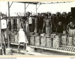 PORT MORESBY, PAPUA. 1944-02-25. NATIVES FILL 4-GALLON DRUMS AT BULK OIL INSTALLATIONS OF THE 1ST PETROLEUM STORAGE COMPANY