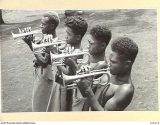 NEW GUINEA. 1943-11-11. CORNET PLAYERS, TOKIEL, KAPI, LEANA AND AMONIA, MEMBERS OF THE NEWLY FORMED BAND OF THE ROYAL PAPUAN CONSTABULARY, AT PRACTICE. THE FIRST NUMBER THEY HAVE MASTERED IS 'GOD ..