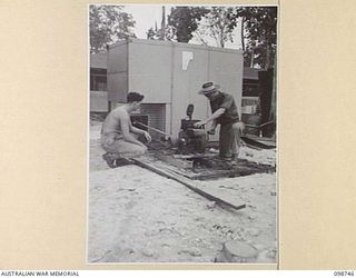 BORAM, NEW GUINEA. 1945-11-16. PRIVATE V. BORCHAM (1) AND PRIVATE W.H. BARBER (2), MEMBERS OF 3 BASE SUB AREA, AUSTRALIAN ARMY CANTEENS SERVICE, START THE MOTOR OF THE REFRIGERATOR WHICH IS USED ..