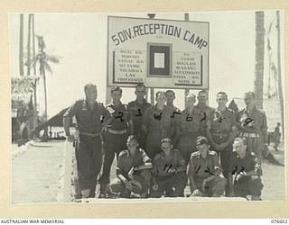 MADANG, NEW GUINEA. 1944-10-18. MEMBERS OF THE STAFF OF THE 5TH DIVISION RECEPTION CAMP IN FRONT OF THE UNIT NOTICE BOARD. IDENTIFIED PERSONNEL ARE:- VX108282 CAPTAIN J.H. SMITH, OFFICER- IN- ..