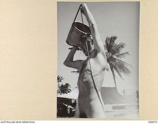 BORAM, NEW GUINEA. 1945-11-21. LIEUTENANT J. FOULDS, 30 INFANTRY BATTALION, USING A CANVAS BUCKET TO TAKE A SHOWER ON THE BEACH