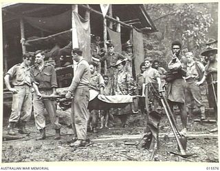 1943-08-16. NEW GUINEA. MOUNT TAMBU. A WOUNDED AMERICAN SOLDIER BEING CARRIED FROM THE ADVANCED DRESSING STATION AT HOUSE BANANA PRIOR TO BEING HANDED OVER TO THE NATIVE BEARERS, KNOWN AS FUZZY ..