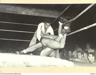 LAE, NEW GUINEA. 1944-07-22. A WRESTLING MATCH IN PROGRESS DURING THE BOXING TOURNAMENT STAGES BETWEEN AUSTRALIAN AND AMERICAN SERVICEMEN. IDENTIFIED PERSONNEL IS:- FIRST SERGEANT MCGRATH, 814TH ..