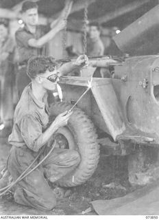 Madang, New Guinea. 1944-06-14. Members of the 266th Light Aid Detachment, Headquarters 15th Infantry Brigade, welding the mudguard of a jeep in the workshop at Siar Plantation. Left to right: ..