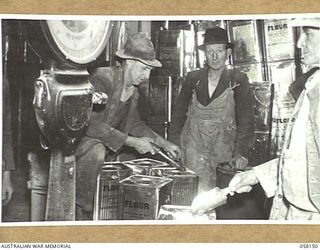 KENSINGTON, VIC. 1943-10-23. WORKMEN AT THE FLOUR MILLS OF MESSRS KIMPTON & SONS CHECKING THE WEIGHT OF FLOUR IN TINS, AFTER WHICH THE LIDS ARE THEN SOLDERED, THE TIN BEING RENDERED AIRTIGHT IN THE ..