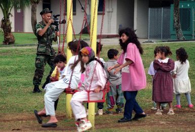 Private First Class Jose Hernandez, of Third Marine Division, Combat Camera, films the children of Marine Forces-operated Tiyan housing annex, Guam as they enjoy the playground during Joint Task Force Operation PACIFIC HAVEN. PACIFIC HAVEN provided over 6,000 pro-US Kurds from Northern Iraq humanitarian assistance and political asylum