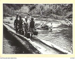 PAPUA, NEW GUINEA. 1942-10. THE COOKS PARTY OF THE 2/33RD AUSTRALIAN INFANTRY BATTALION BRINGING THE WATER RATION ACROSS A HUGE LOG SPANNING A RIVER BETWEEN NAURO AND MENARI