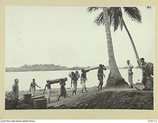 MILILAT, NEW GUINEA. 1944-08-07. NX67711 LANCE CORPORAL C.E. SIMPSON, MILITARY LANDING OFFICER, HEADQUARTERS, 5TH DIVISION SUPERVISING THE NATIVES UNLOADING SUPPLIES FROM BARGES AT THE BRIDGEHEAD. ..